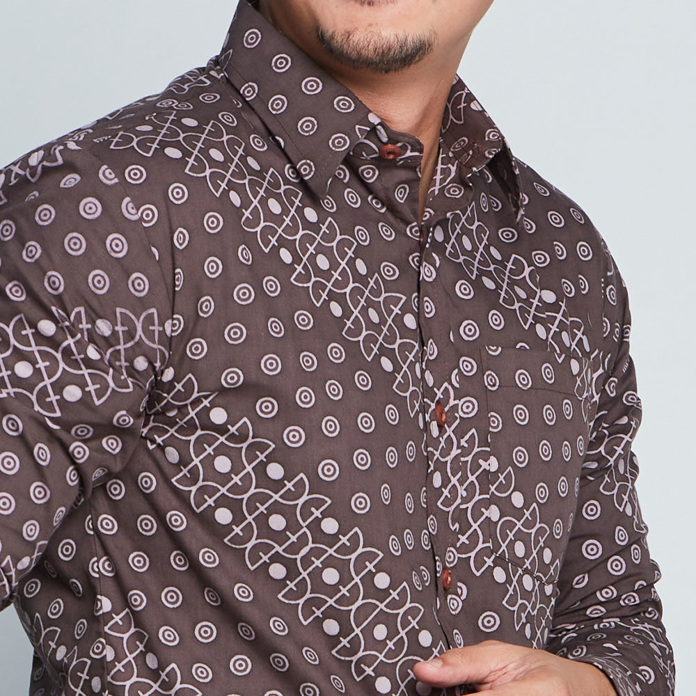 a close-up view of a man wearing a batik shirt in brown alur in front of a white wall