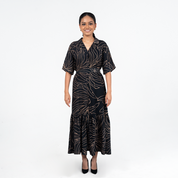 Front view of Batik Boutique’s Onyx Palma Button-Up Dress in black with soft gold botanical lines, styled with a flattering waist tie
