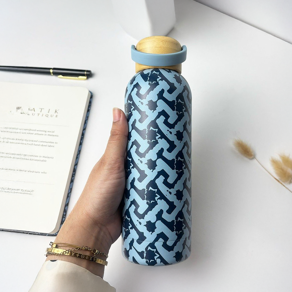 Hand holding a midnight arabesque  patterned water bottle with a wooden cap on a white surface.