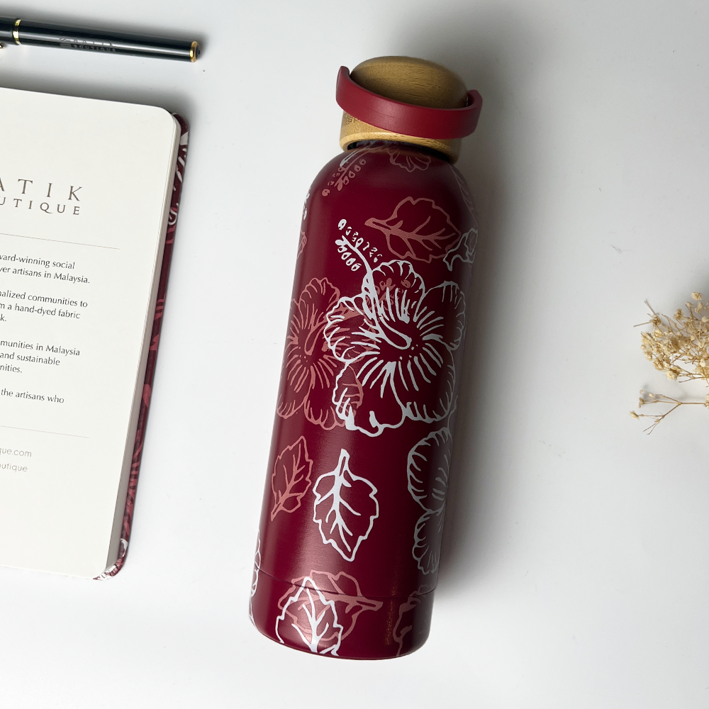 Red water bottle with floral design on a white surface with a book and pen.
