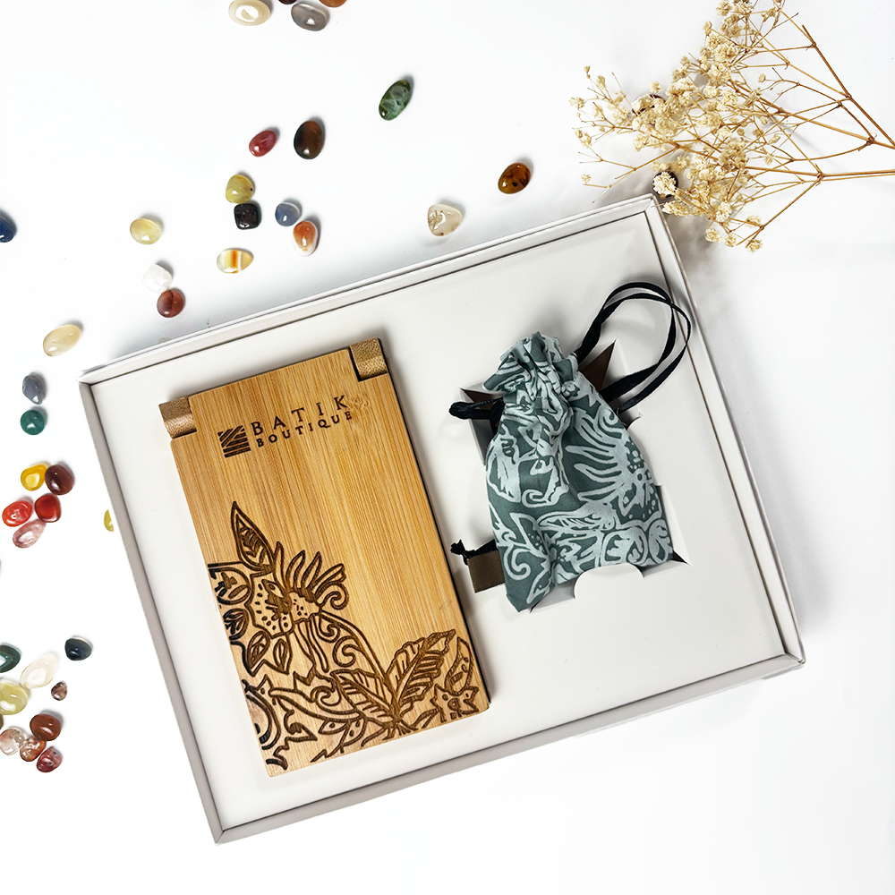 Batik Boutique Congkak Gift Set featuring bamboo congkak board engraved with floral batik motif and sage green batik pouch, presented in white gift box surrounded by decorative stones.