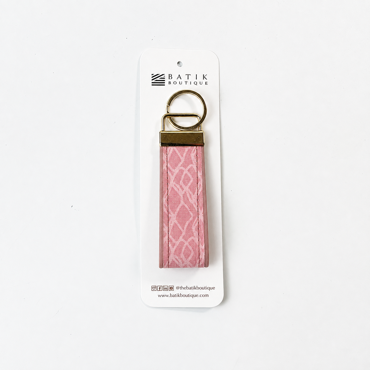 A pink patterned fabric keychain with a gold metal ring and connector, attached to a white cardboard hanger labeled 'BATIK OUTLETTE'.