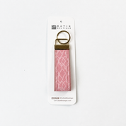 A pink patterned fabric keychain with a gold metal ring and connector, attached to a white cardboard hanger labeled 'BATIK OUTLETTE'.