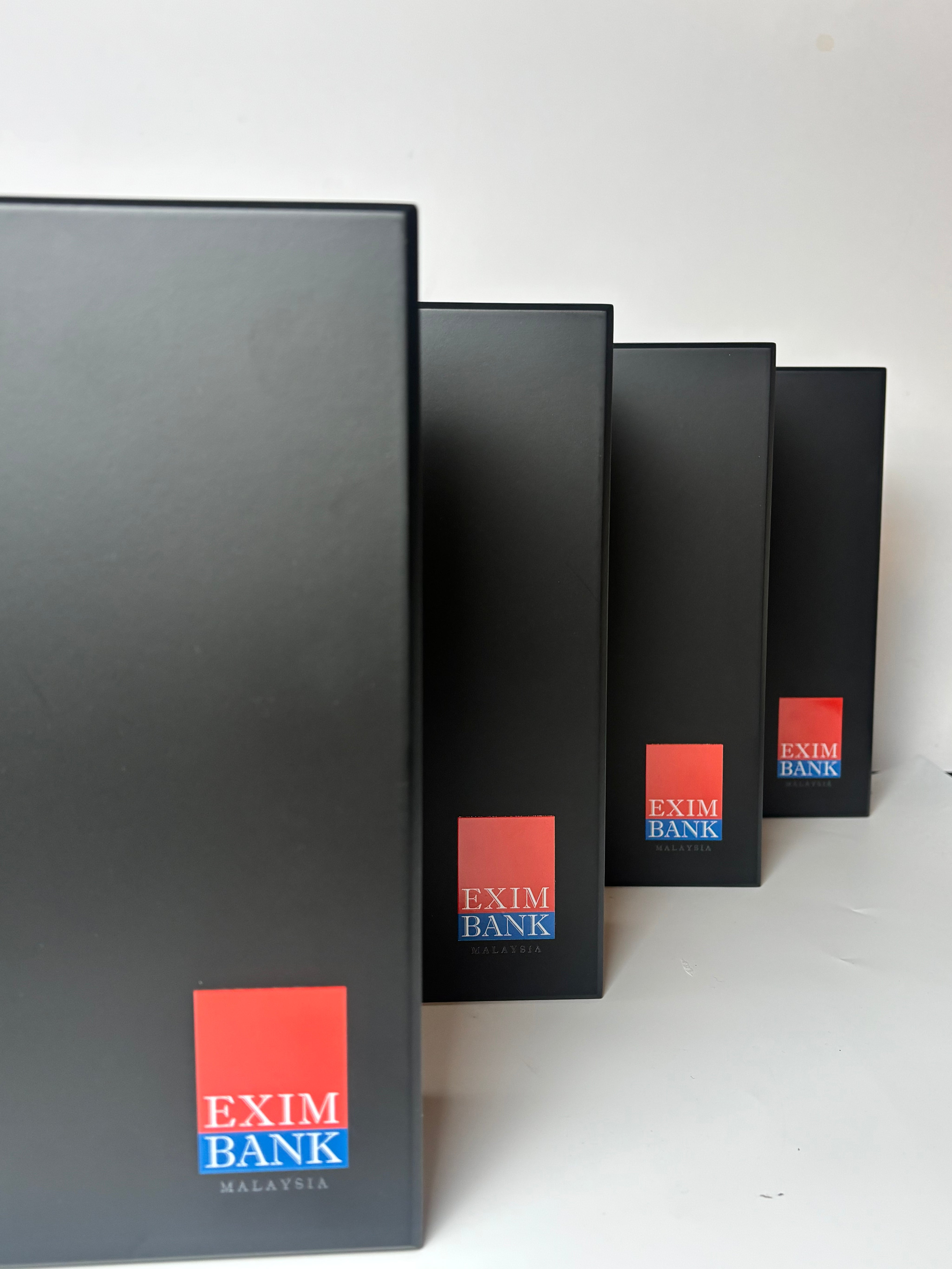 Four black binders with Exim Bank Malaysia logo on a white background