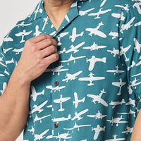 a man in front of a white wall wearing a batik shirt in the pattern turquoise airplane