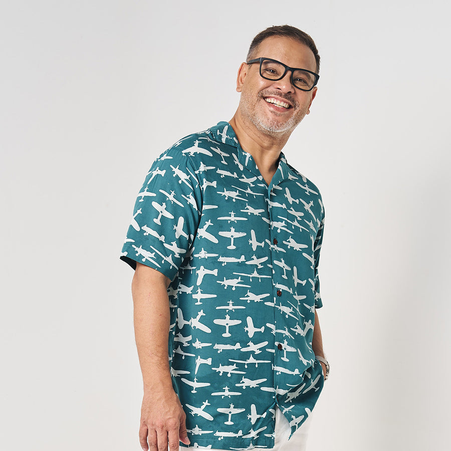 a man in front of a white wall wearing a batik shirt in the pattern turquoise airplane