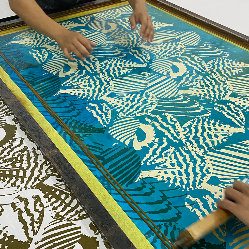 Person using a screen printing technique with a blue and yellow pattern on a wooden screen.