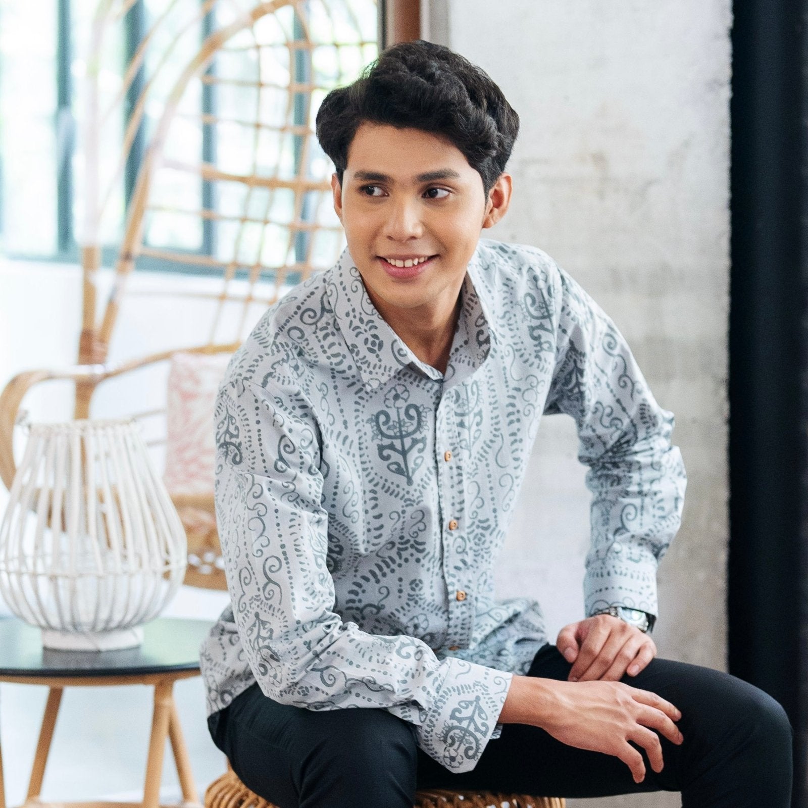 model wearing the Men's Long-Sleeved Batik Shirt Grey Petola sitting on a stool 
