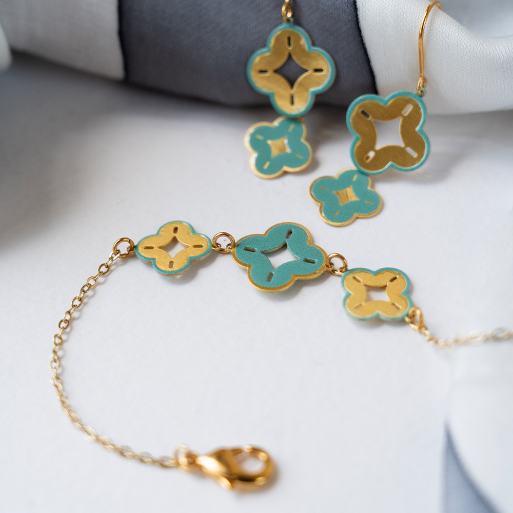 Flat lay of turquoise and gold floral charm bracelet with matching earrings on white fabric.