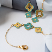 Flat lay of turquoise and gold floral charm bracelet with matching earrings on white fabric.