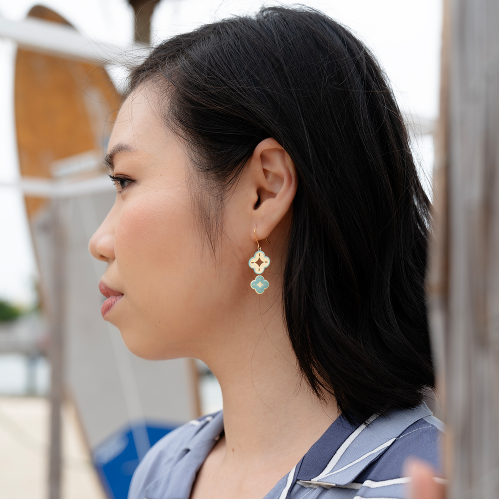 Woman wearing gold geometric earrings with modern batik print shirt, outdoors.