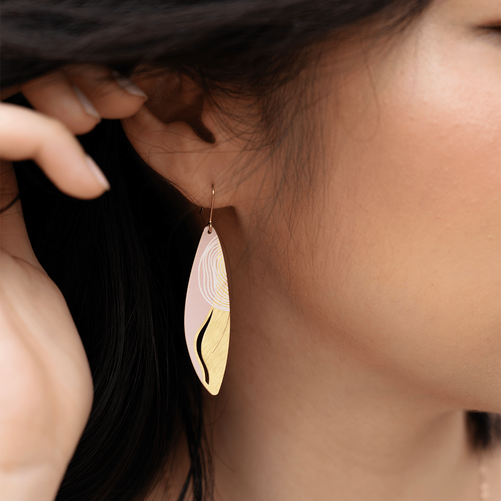 Model wearing a gold and blush pink leaf-shaped earring with wavy line details.
