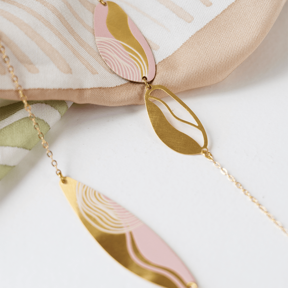 Close-up of a gold and pink batik-inspired pendant necklace with abstract detailing on soft batik fabric.