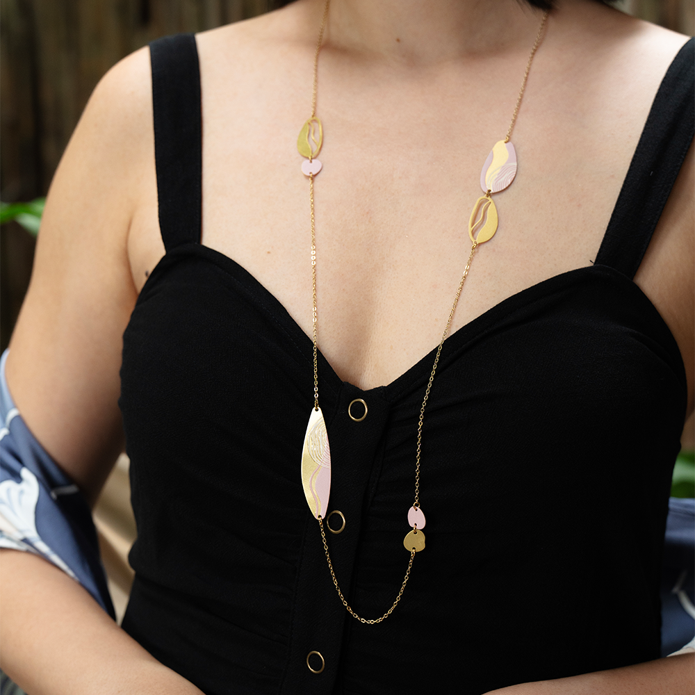 Model wearing a long gold necklace with pink and gold batik-inspired charms over a black top.