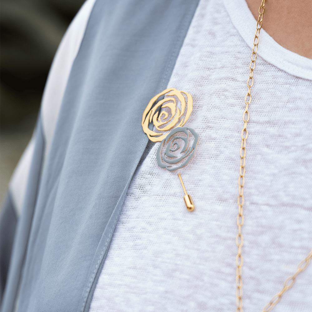 Gold and silver rose brooches styled together on a white knit top and grey outerwear, accessorized with a gold necklace.