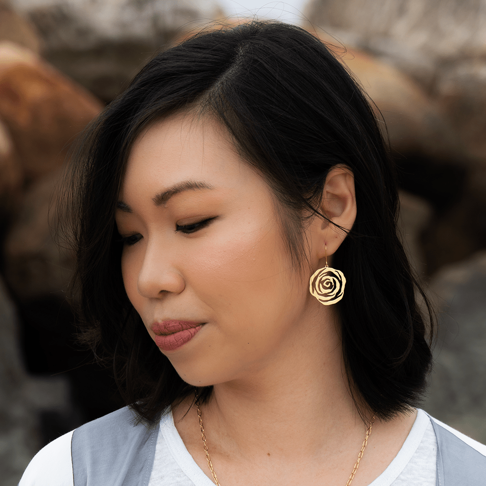 woman wearing a single gold rose-shaped earring with soft curls and minimal makeup.