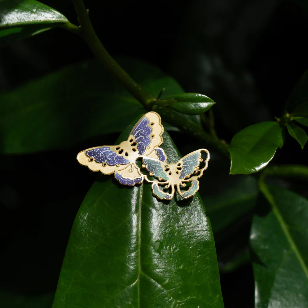 Butterfly-shaped pins on a green leaf with a dark background