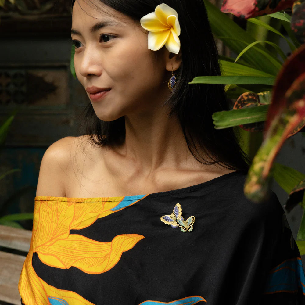 Woman wearing a black top with yellow and blue floral patterns, standing in a natural setting.