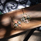 Pair of gold earrings with colorful square designs on a wooden surface