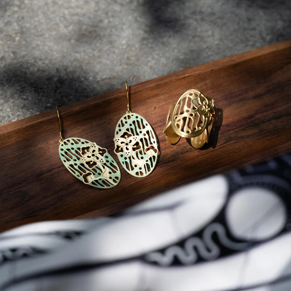 Pair of gold and green earrings on a wooden surface with a blurred background