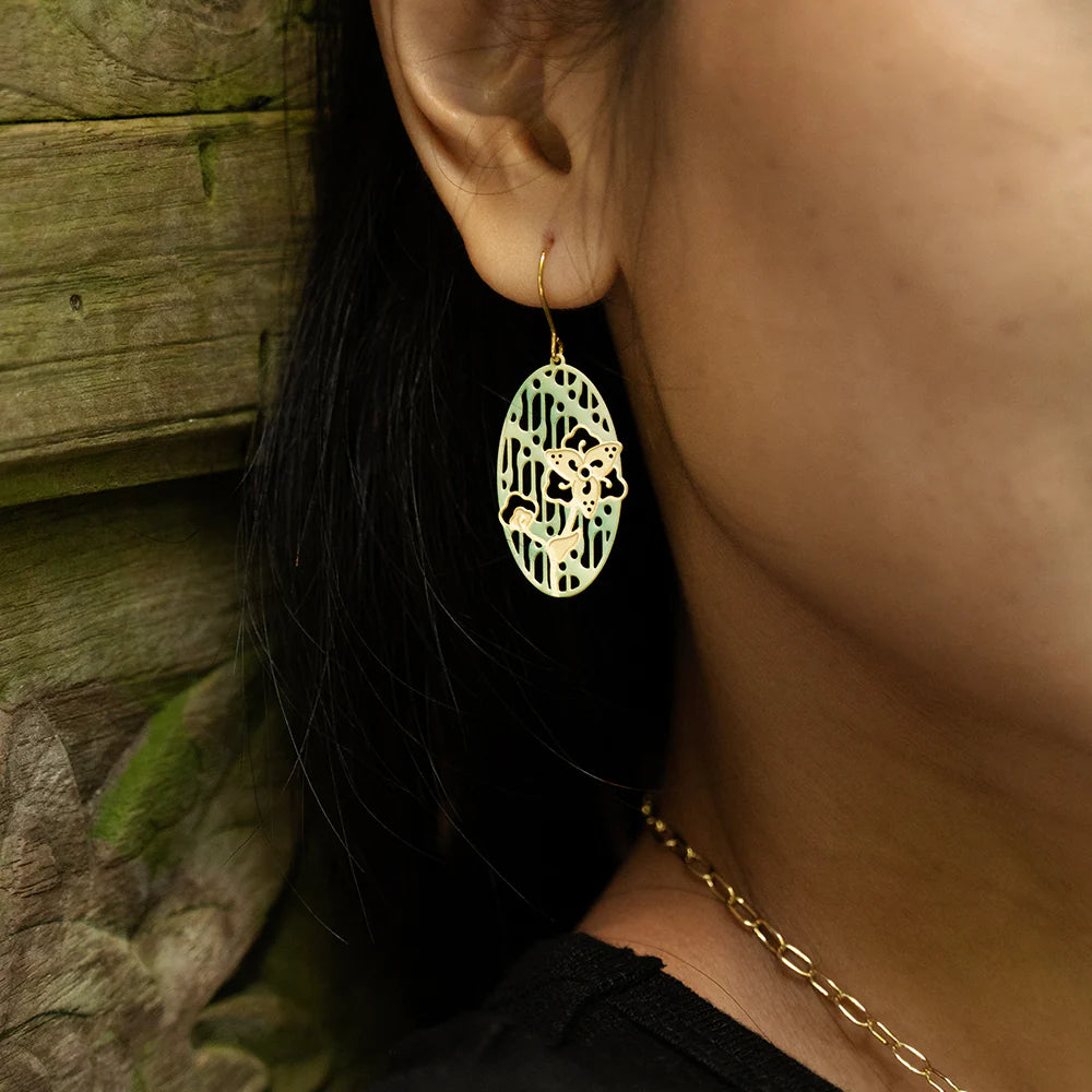 Close-up of a person wearing a gold earring with a detailed design, against a natural background.