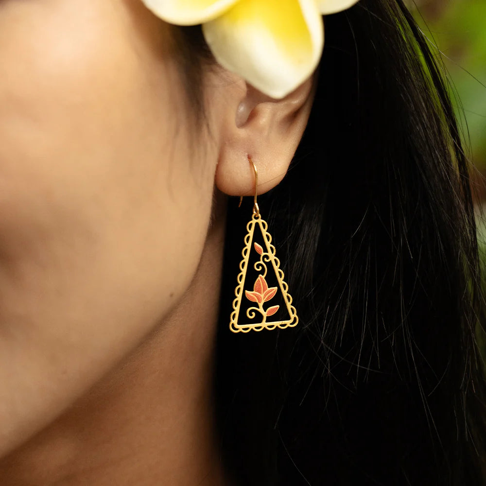Close-up of a person wearing a gold triangle-shaped earring with a floral design, against a blurred background.