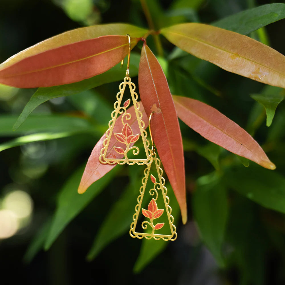 Gold leaf-shaped earrings hanging on a branch with green leaves.