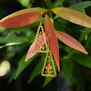 Gold leaf-shaped earrings hanging on a branch with green leaves.