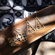 Pair of decorative earrings on a wooden surface with a patterned fabric background