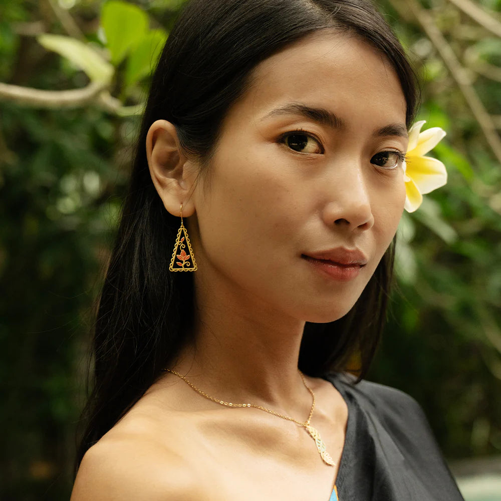 Woman with a flower in her hair, wearing gold jewelry, against a green foliage background