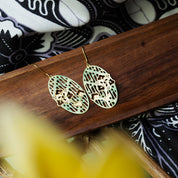 Gold earrings on a wooden surface with a patterned fabric background