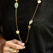 Gold necklace with floral pendants held by a hand against a black background