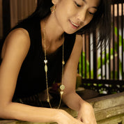 Woman wearing a long gold necklace with beads in a blurred indoor setting