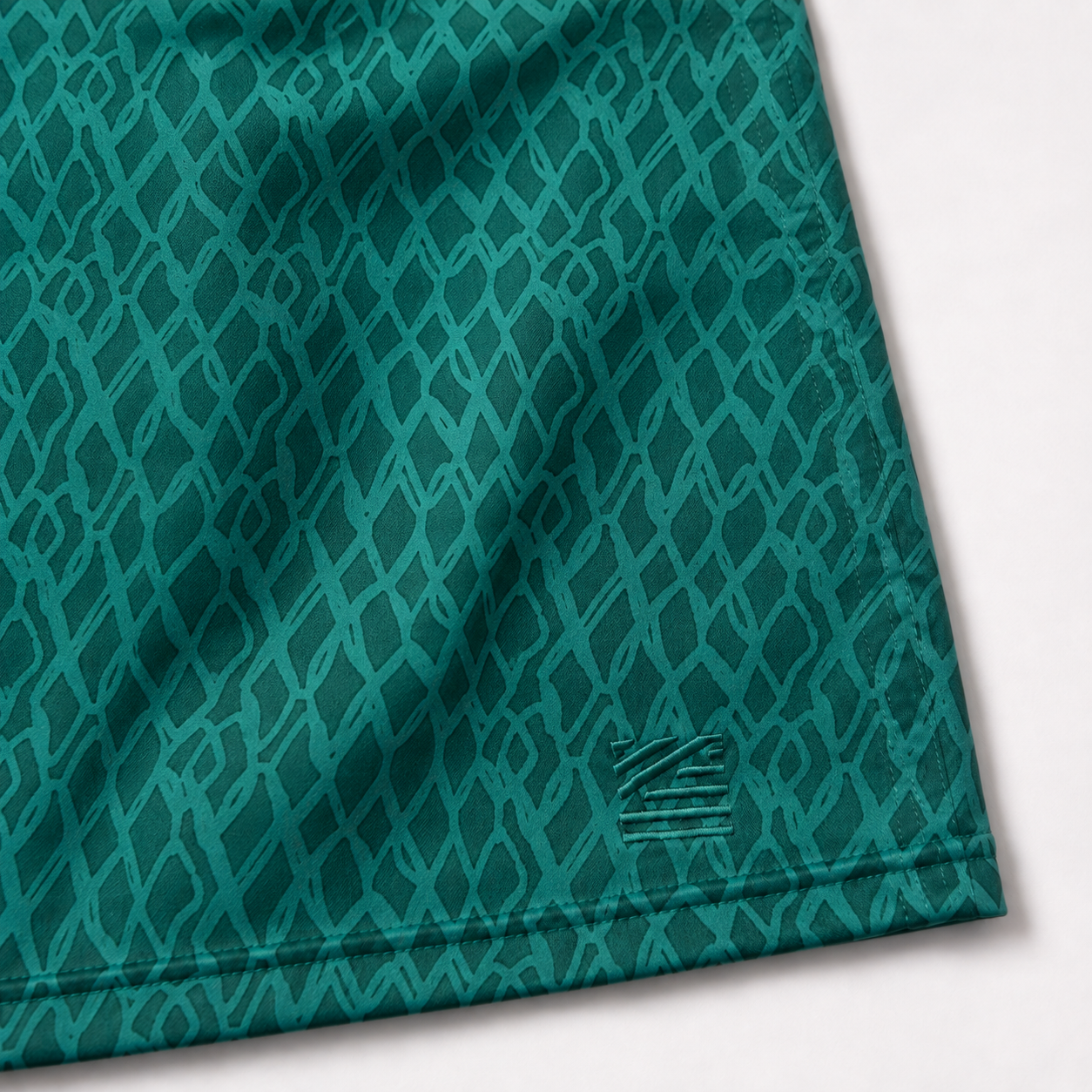 Close-up of a teal athletic fabric with a repeating diamond pattern and a small woven logo near the lower right corner, shown on a white background.