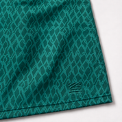 Close-up of a teal athletic fabric with a repeating diamond pattern and a small woven logo near the lower right corner, shown on a white background.
