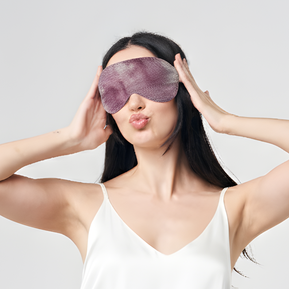 Woman wearing Batik Boutique plum shibori eye mask, smiling playfully in white camisole against neutral background.