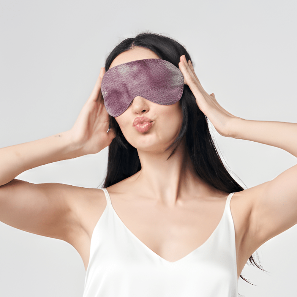 Woman wearing Batik Boutique plum shibori eye mask, smiling playfully in white camisole against neutral background.