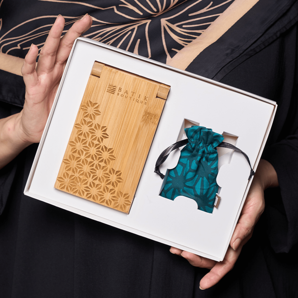 a woman holding a congkak set with laser engraved congkak board and batik pouch in the pattern forest firework