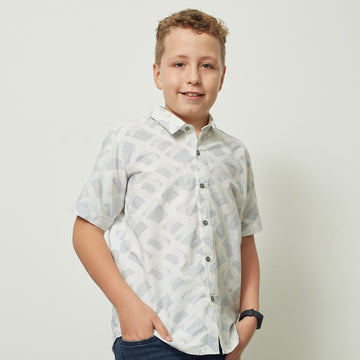 a boy standing in front of a white wall while wearing a grey nasi lemak batik shirt