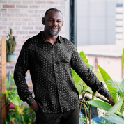Model in the Black Alur batik shirt standing by plants in an urban setting, displaying the shirt’s casual yet refined style.