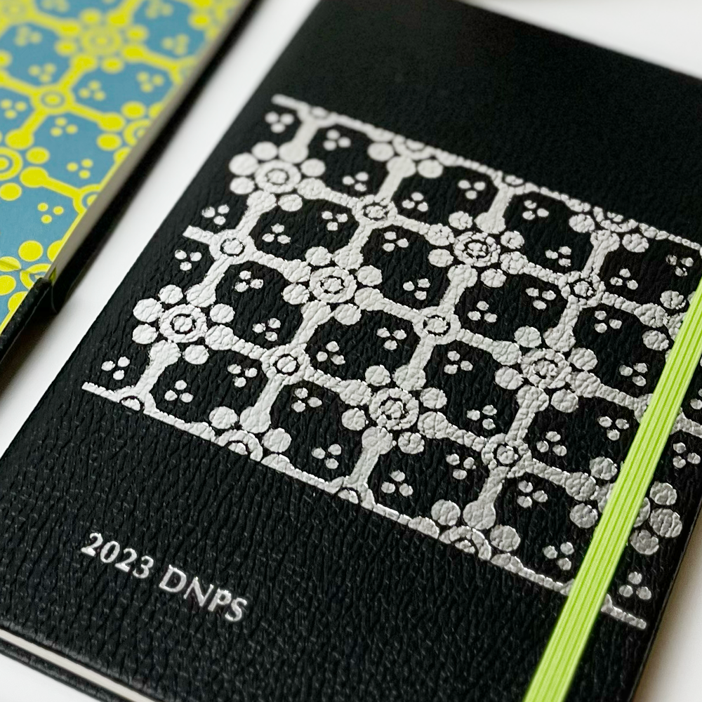 Black notebook with silver floral pattern and '2023 DNPS' text on a white background