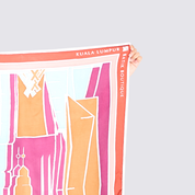 A hand holds up a square scarf featuring a colorful abstract cityscape design with the text 'KUALA LUMPUR BIK BOUTIQUE' and 'BAIK BOUTIQUE' printed along the border, set against a solid light gray background.