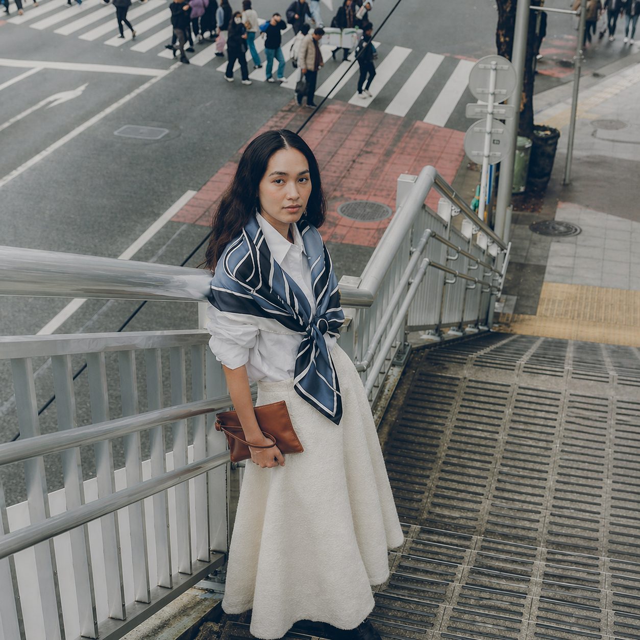 Woman in a white dress with a blue scarf standing on a city street.