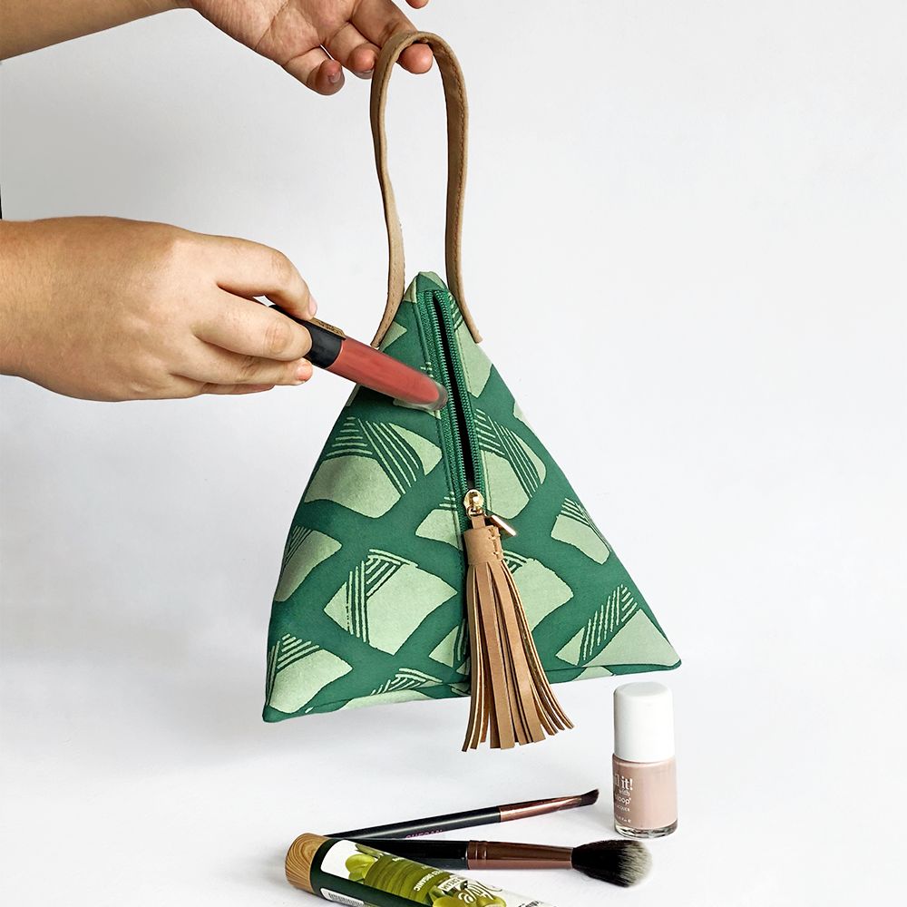 a photo showcasing a ketupat bag made of batik in the pattern green nasi lemak accompanied by props in front of a white background