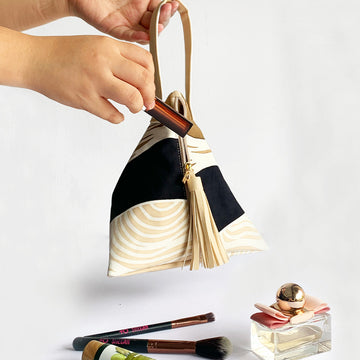 a lifestyle photo of batik ketupat bag in midnight bukit showing a woman hand holding the bag while insert lipstick in the bag
