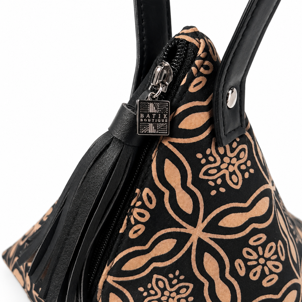 Close-up of a black handbag with a tan floral and paisley pattern, black leather handles, a black leather tassel zipper pull, and a silver-tone metal brand plaque reading 'MATIX BOUTIQUE'.