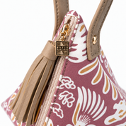 Close-up of a maroon handbag with a tan floral and paisley pattern, tan leather handles, a tan leather tassel zipper pull, and a gold-tone metal brand plaque reading 'BATIK BOUTIQUE'.