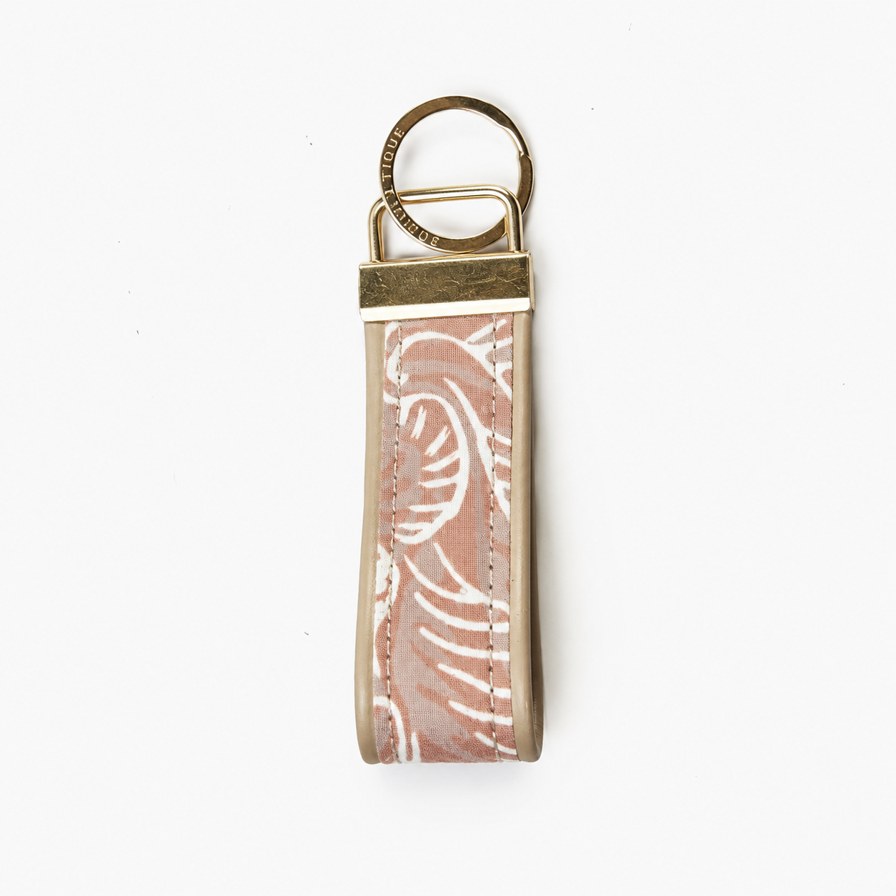 A rectangular keychain or key tag with a dusty pink and white patterned strap, finished with brass-toned metal hardware and a split key ring, shown on a plain white background.