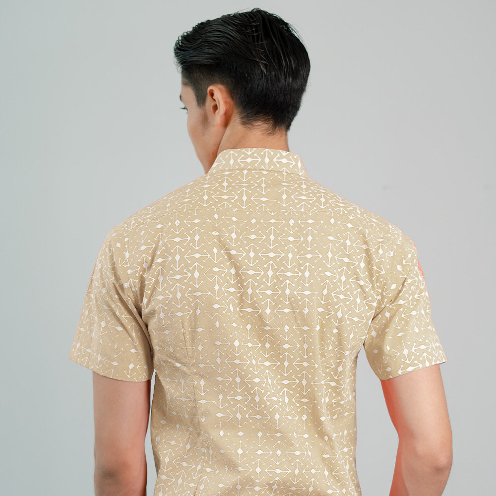 a back shot of a man standing in front of a white wall in latte kompas batik shirt from batik boutique