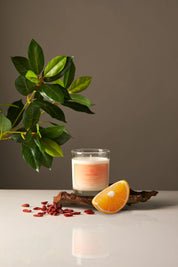 Candle in a glass jar with an orange wedge and leaves on a neutral background